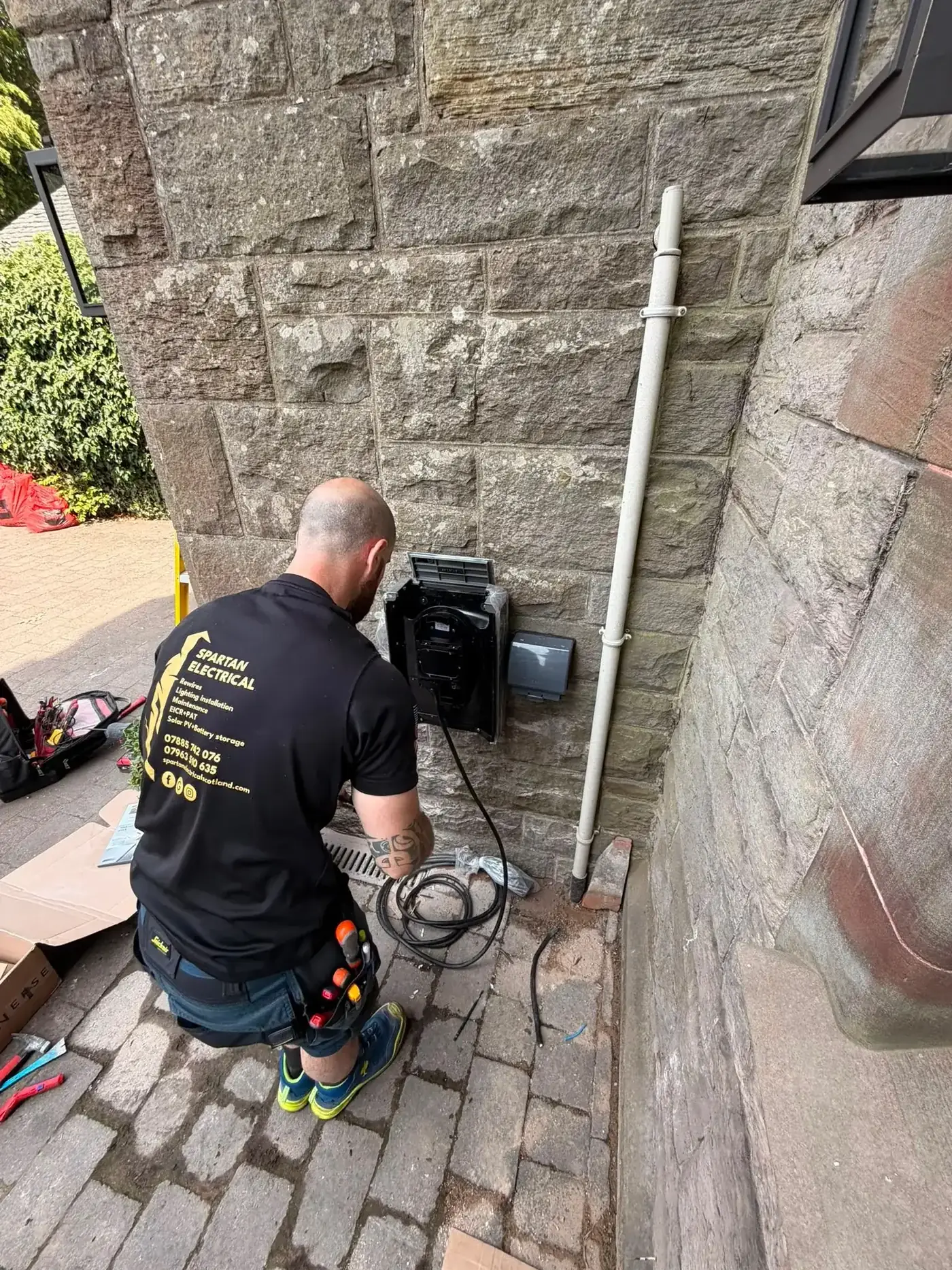 Spartan Electrical engineer wiring an EV charger, tool belt and cables on the ground